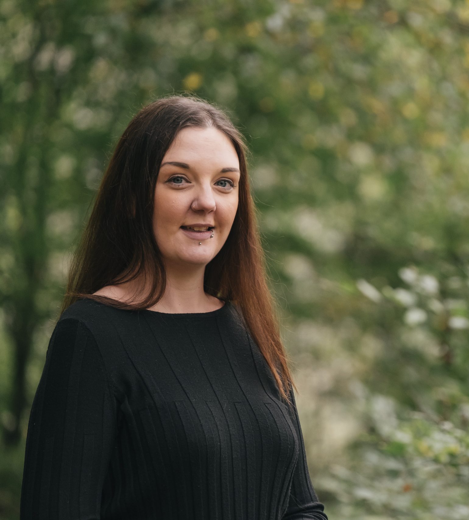 Sarah Hutt, founder of Wild Rose Path, smiling outdoors surrounded by greenery.